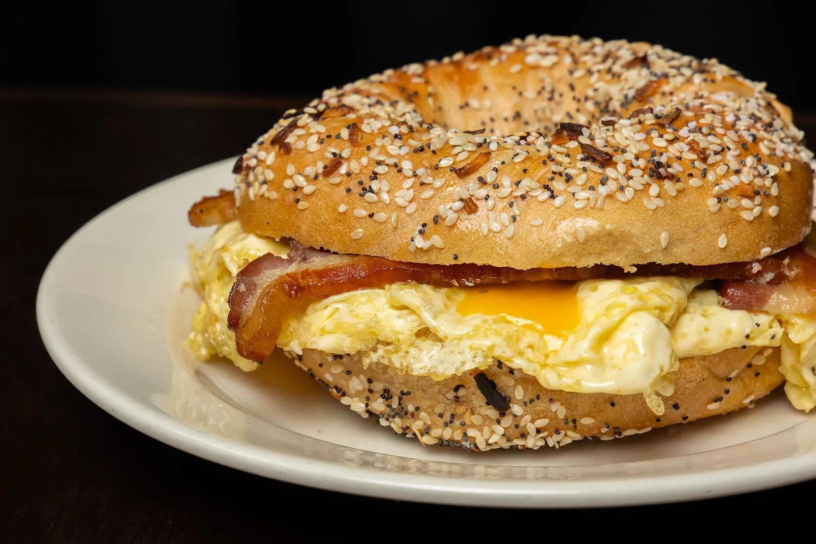 Bacon, egg and cheddar on an everything bagel, served on a white plate