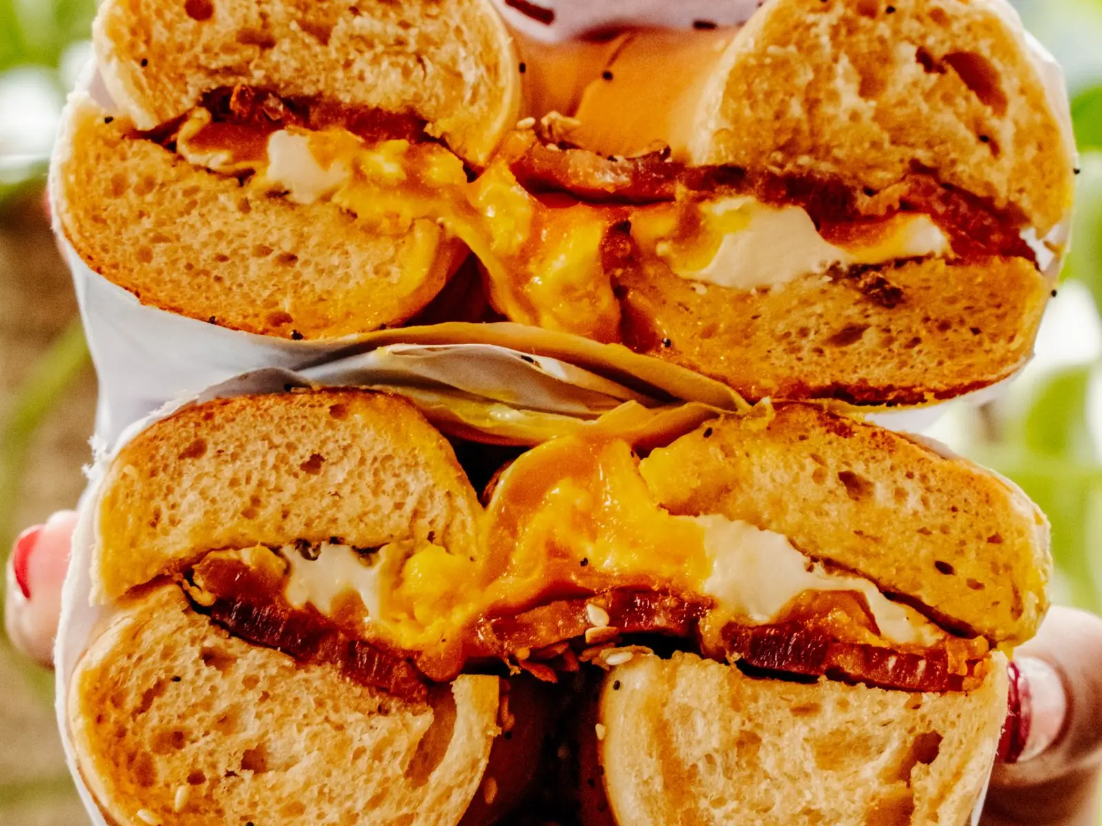 Bacon, egg and cheddar bagel sandwich cut in half and stacked, melted cheddar and thick-cut bacon showing