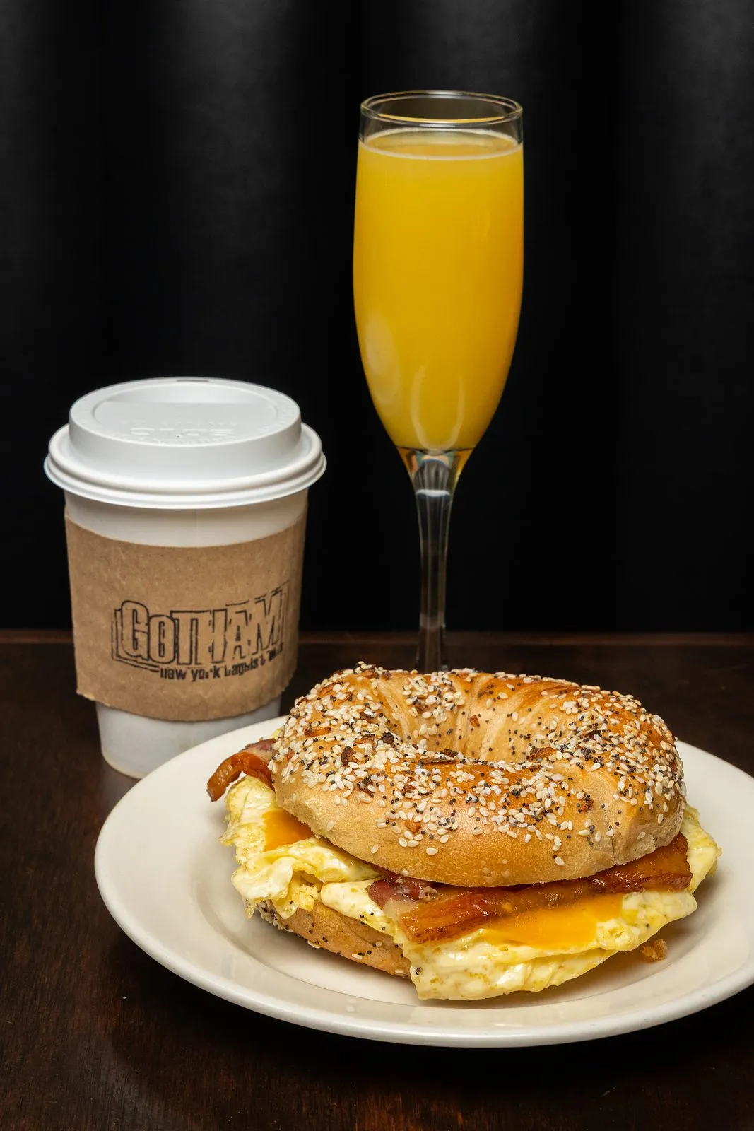 A bacon, egg and cheese bagel with a Gotham coffee and a glass of orange juice