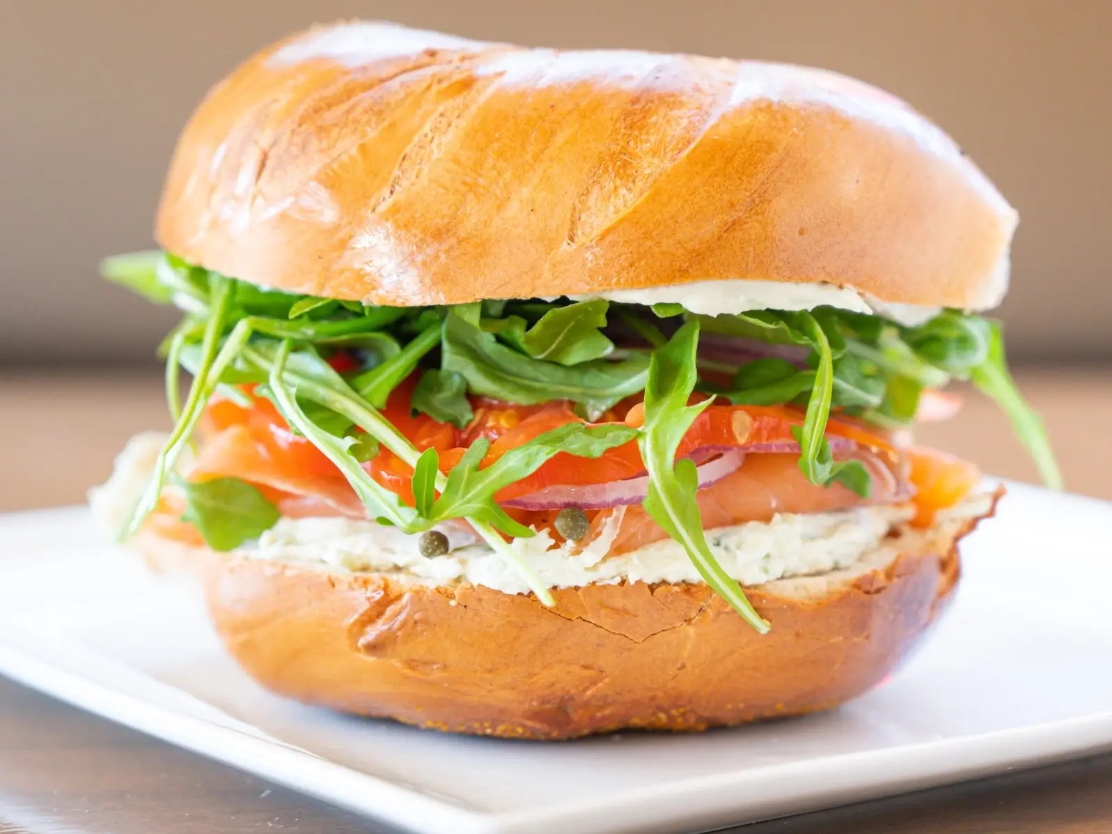 The Brighton Beach: cold-smoked salmon, cream cheese, arugula, heirloom tomato, red onion and capers on a plain bagel, on a white plate