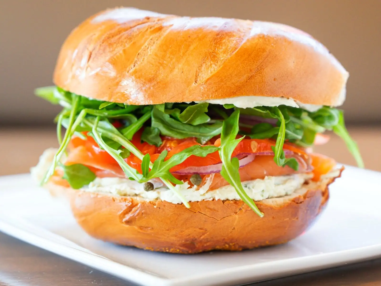 The Brighton Beach: cold-smoked salmon, cream cheese, arugula, heirloom tomato, red onion and capers on a plain bagel, on a white plate