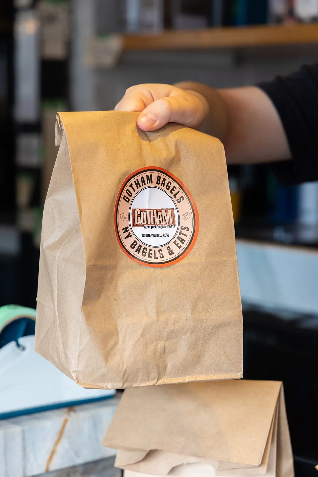 A Gotham Bagels carryout bag handed across the counter