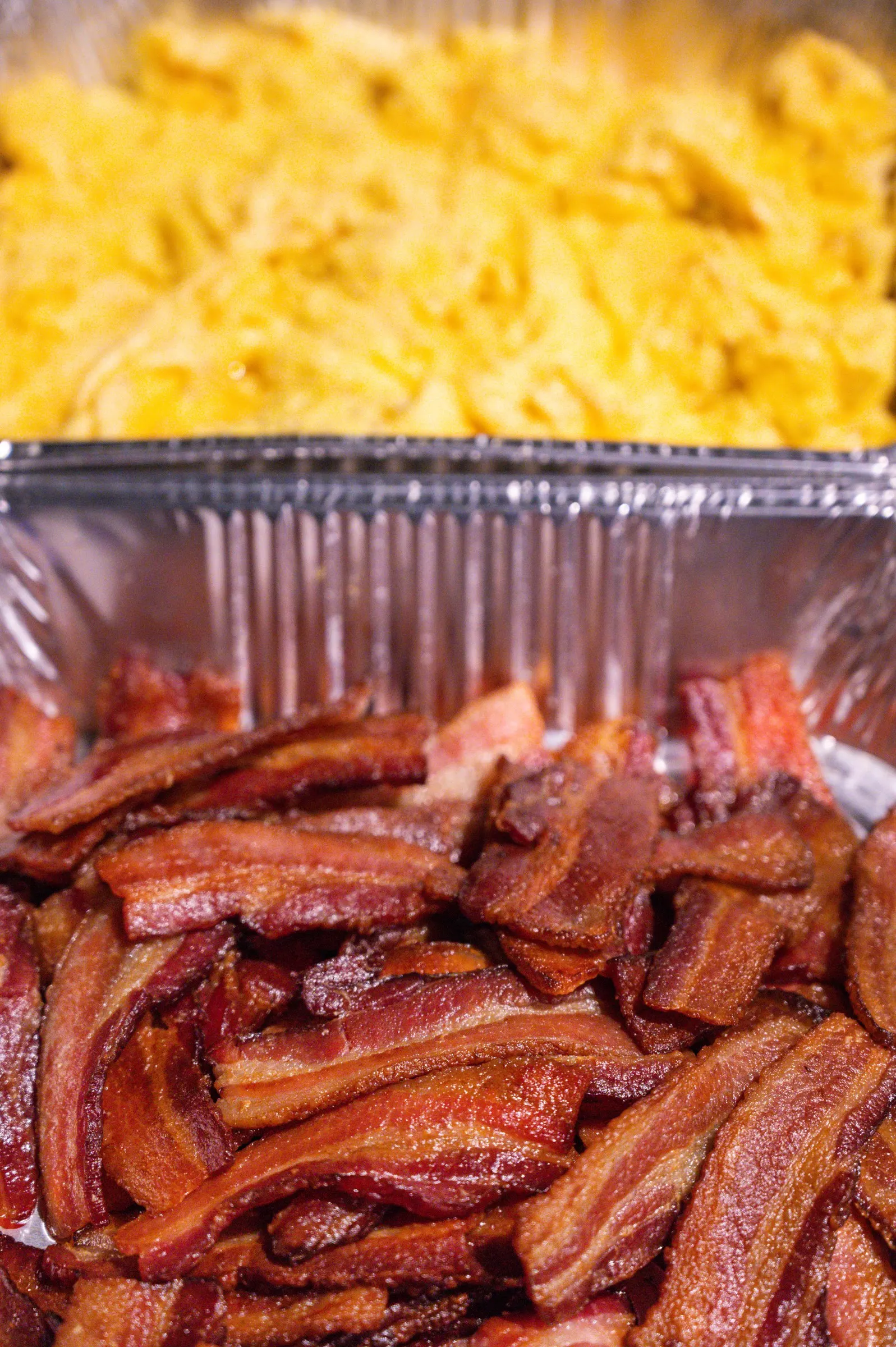 Half pans of scrambled eggs and crisp bacon, ready for a catered breakfast
