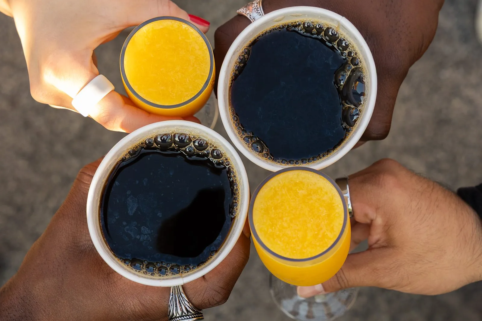 Four hands toasting with cups of black coffee and orange juice, seen from above