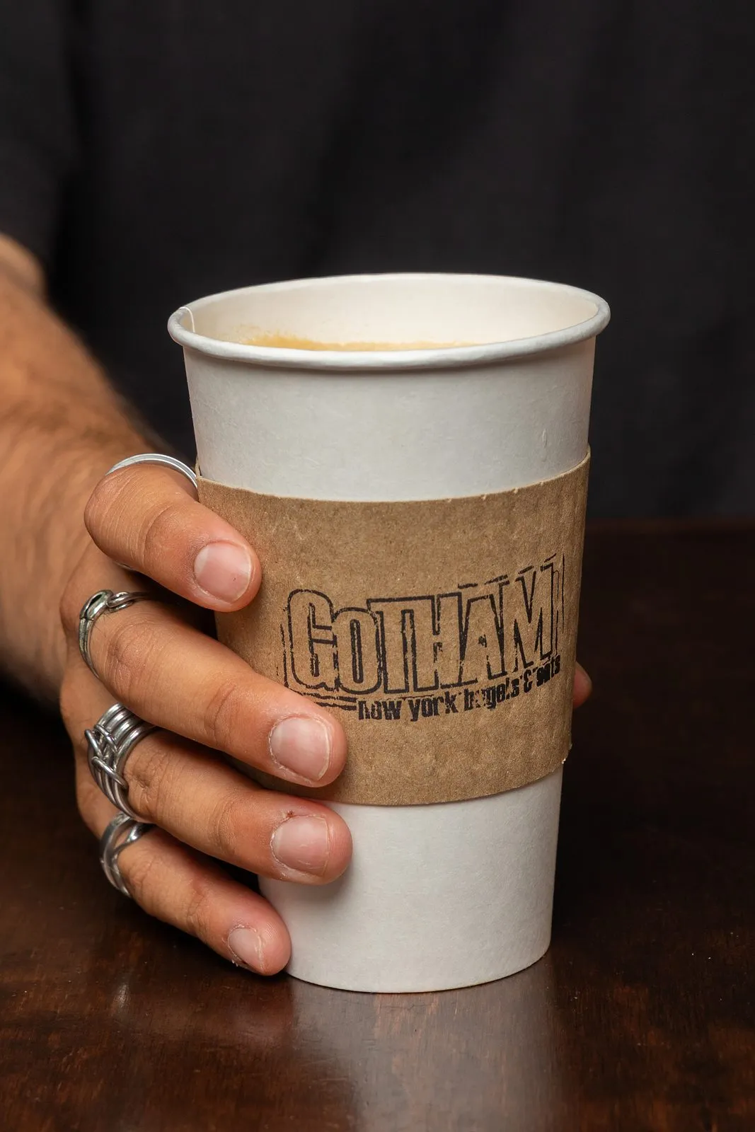 A hand holding a hot coffee in a Gotham Bagels cup sleeve