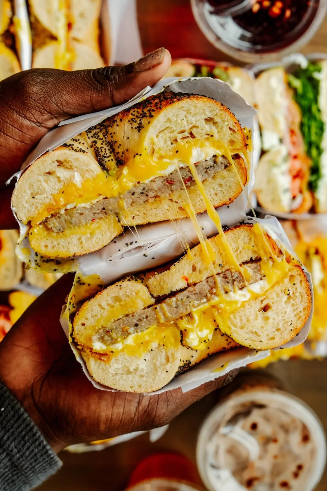 A sausage, egg and cheese on a poppy bagel, cut in half and held up with the cheese pulling between the halves