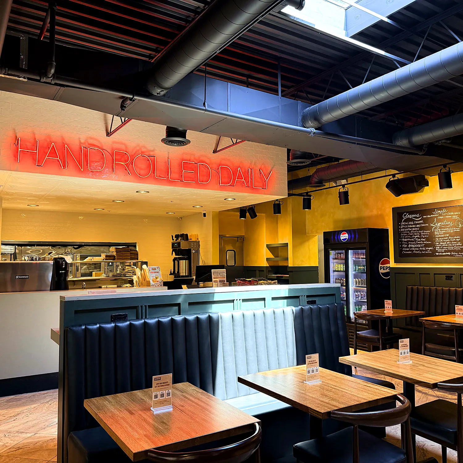 Inside Gotham Bagels Lake Geneva, with the Hand Rolled Daily neon over the counter