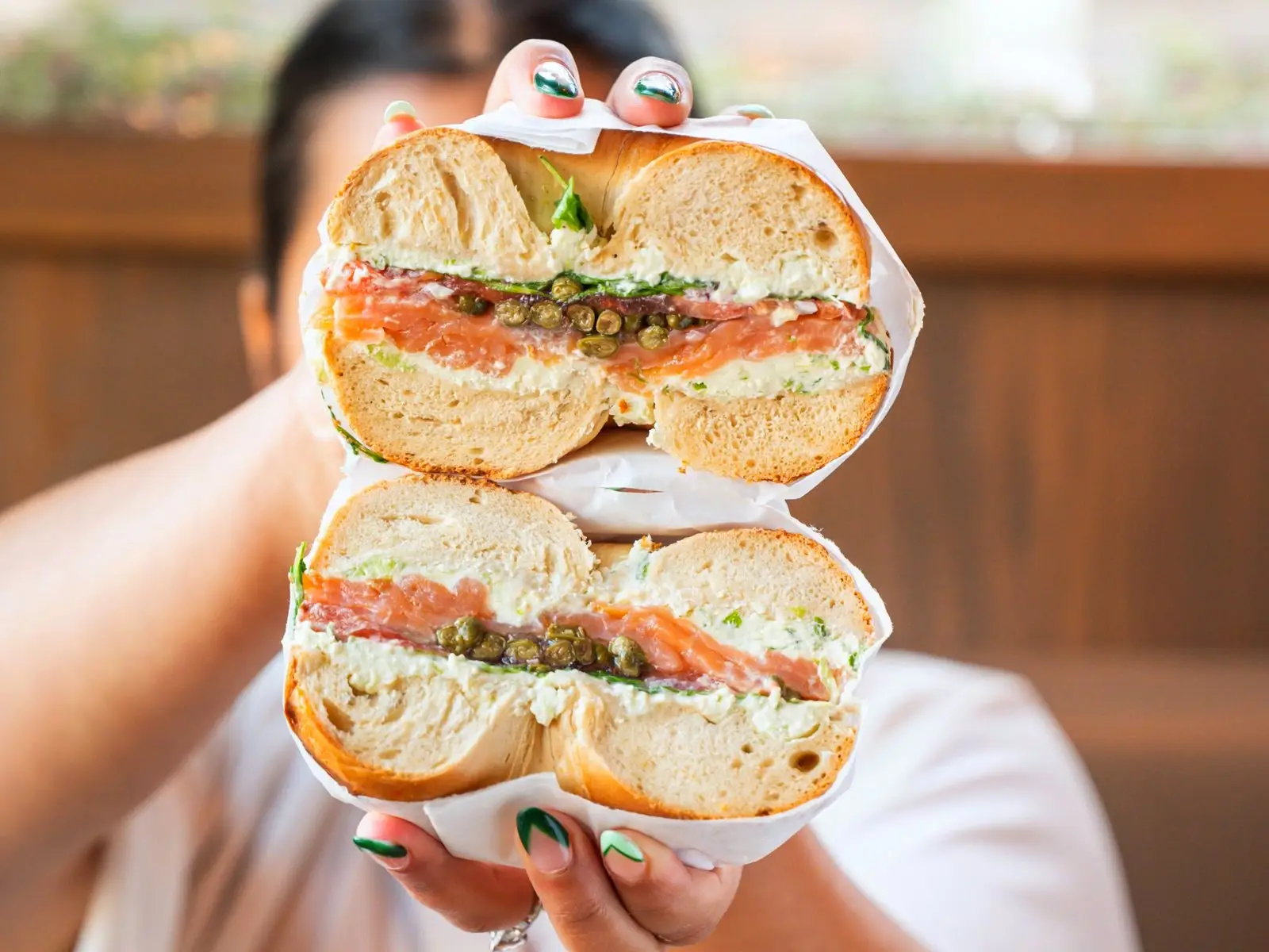 Lox and cream cheese bagel sandwich with capers, cut in half and held up to the camera