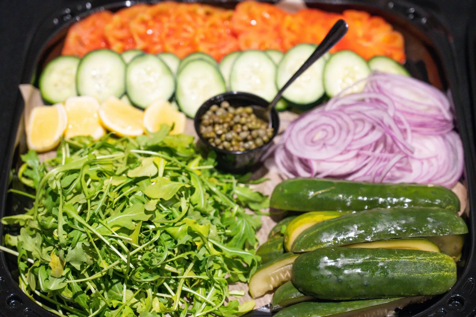 Gotham lox platter from above: cold-smoked salmon, sliced cucumber, lemon, capers, red onion, arugula and pickles