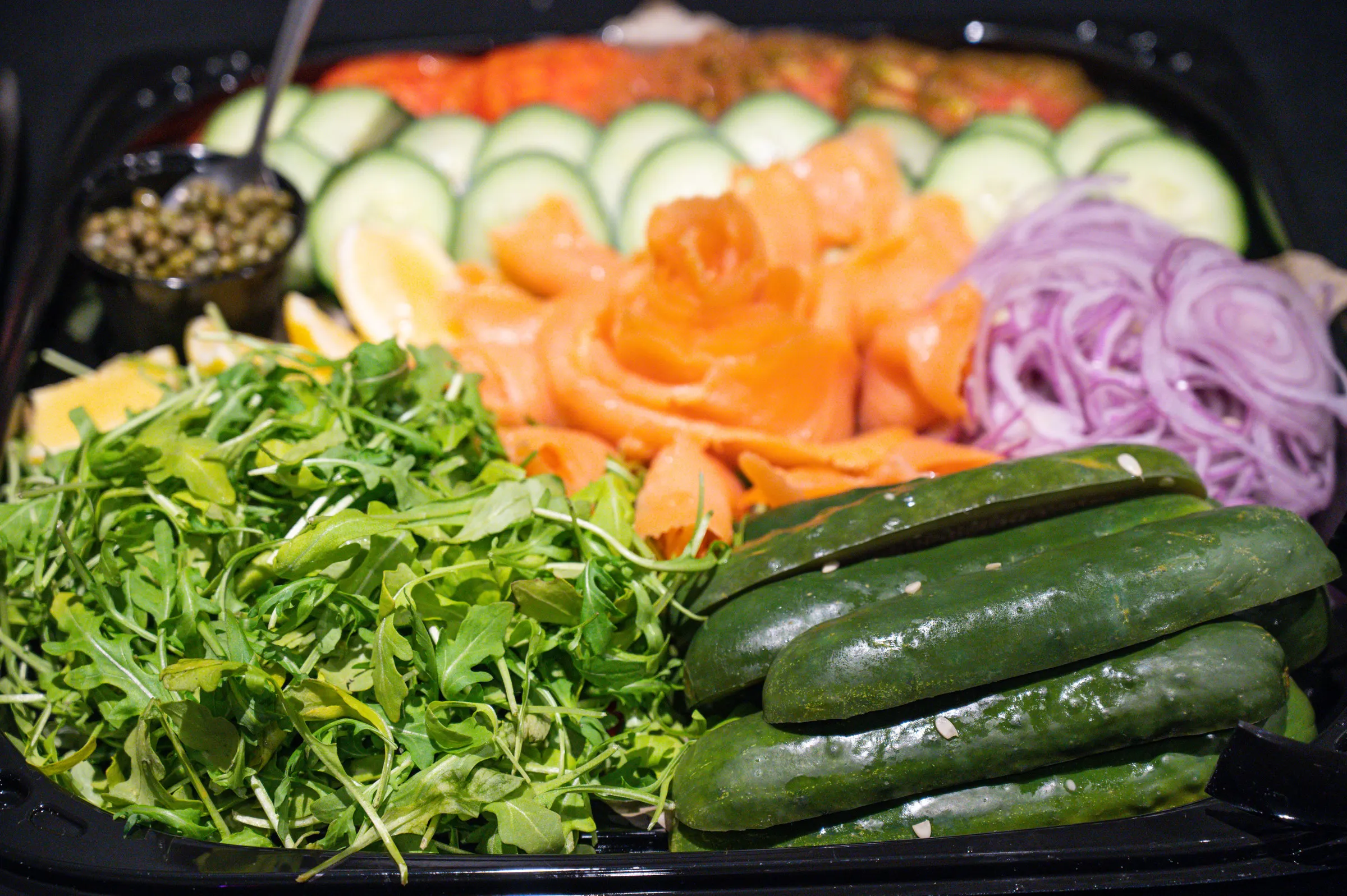 Gotham lox platter from above: cold-smoked salmon, sliced cucumber, lemon, capers, red onion, arugula and pickles