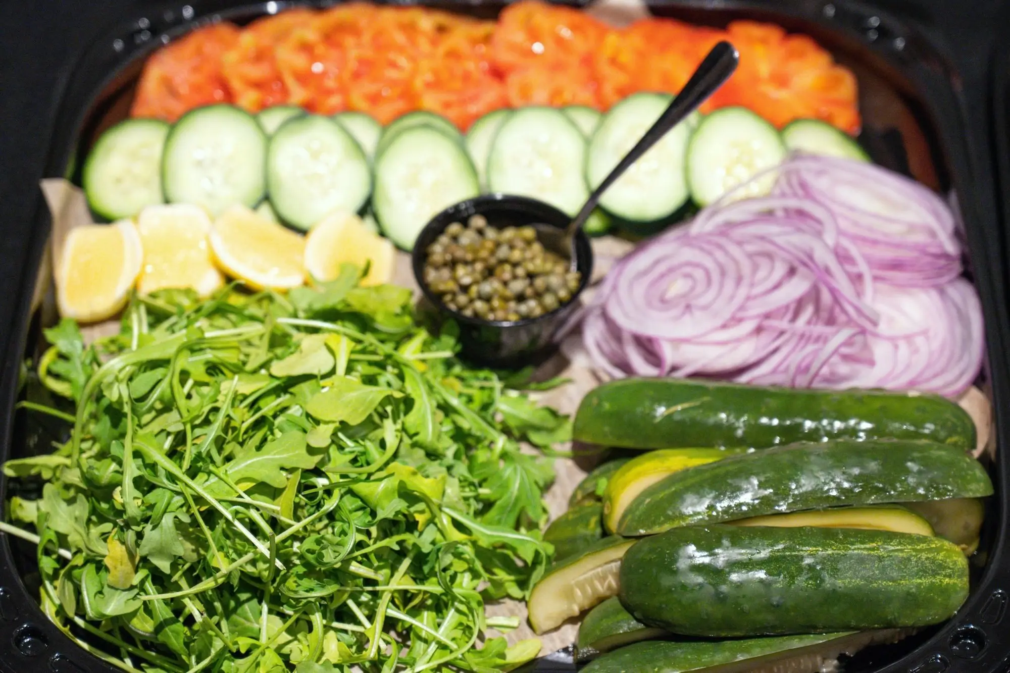 Gotham lox platter from above: cold-smoked salmon, sliced cucumber, lemon, capers, red onion, arugula and pickles
