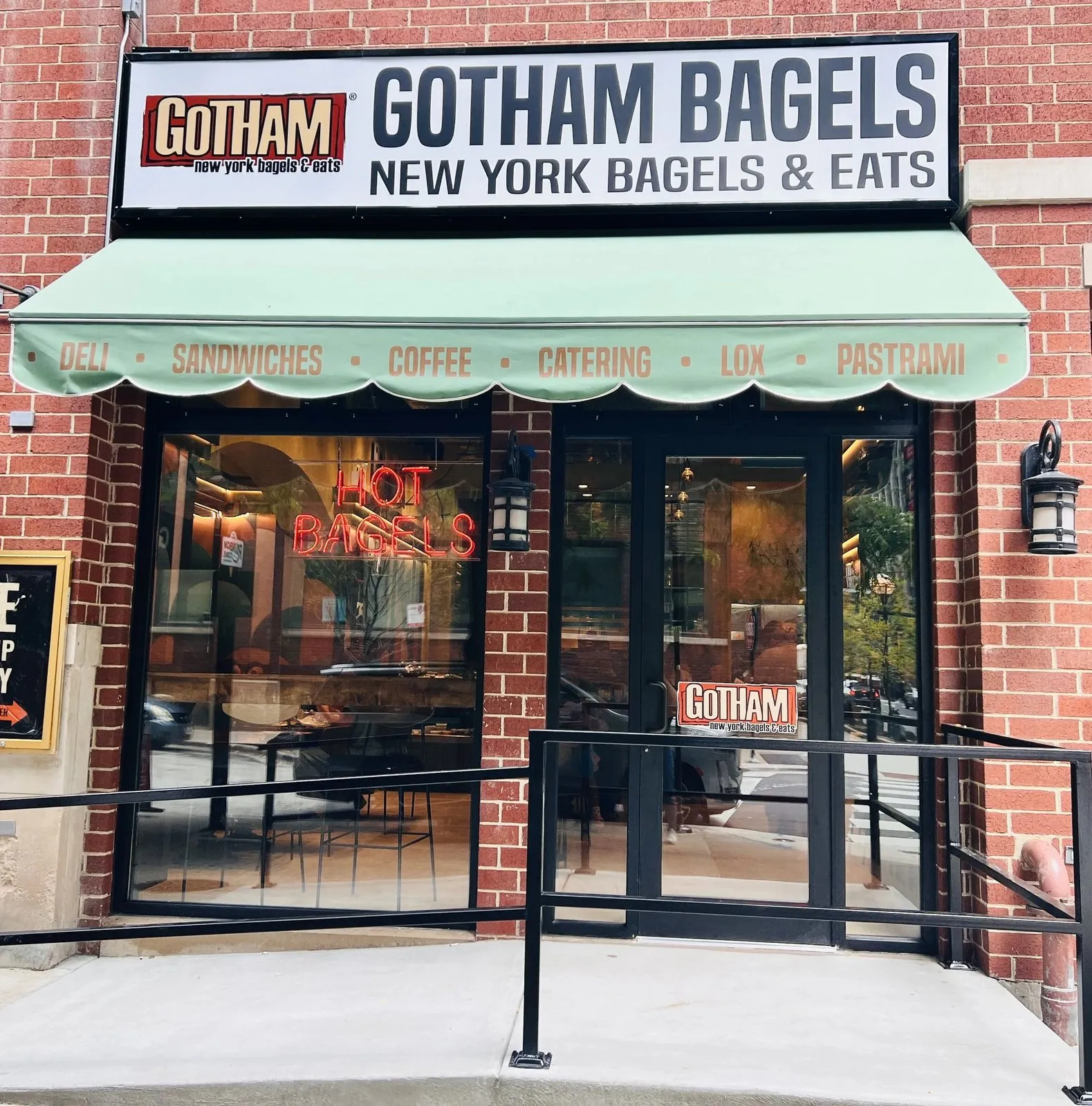 Gotham Bagels Magnificent Mile storefront on E Superior St, with a green awning and Hot Bagels neon in the window