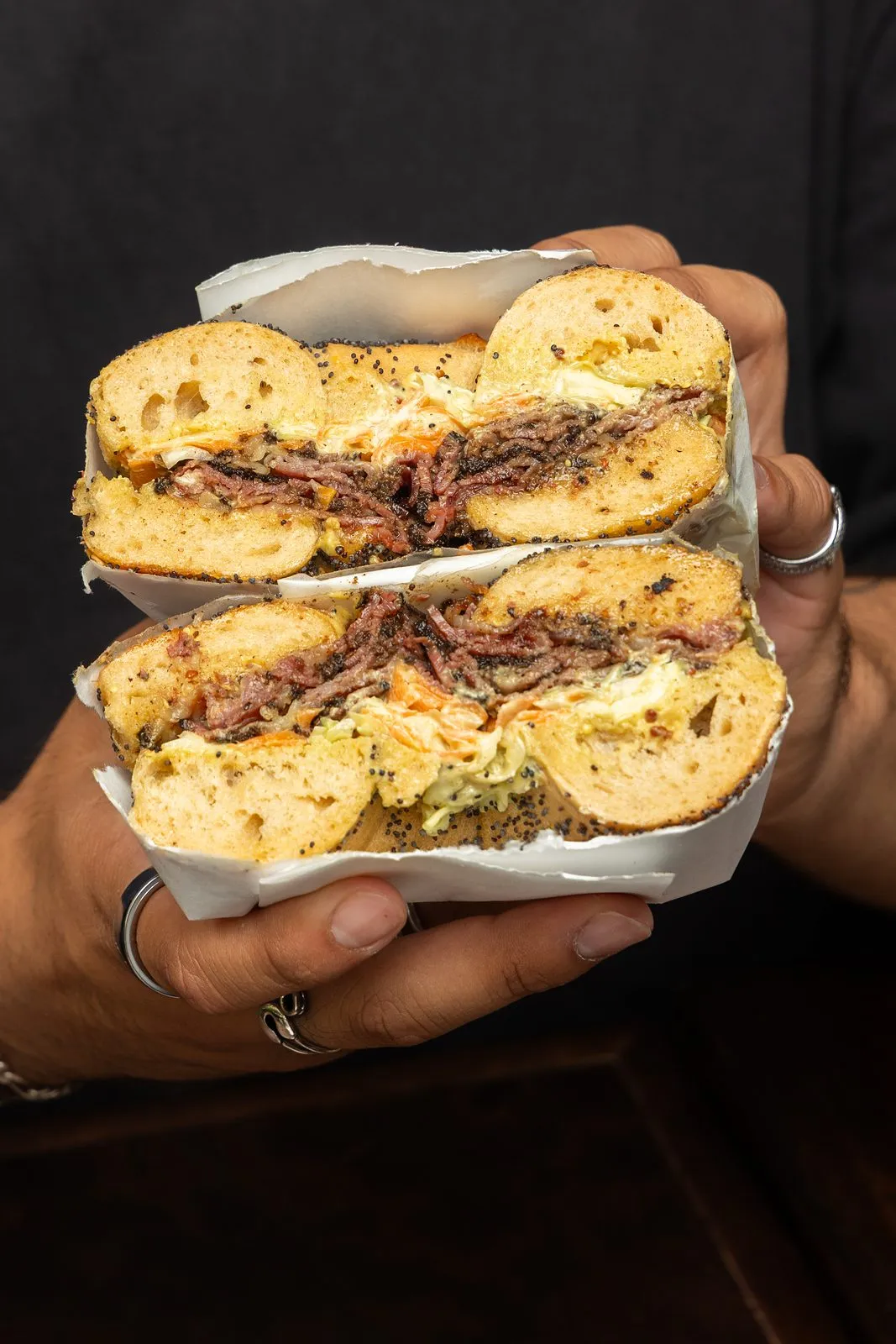 A pastrami and egg bagel sandwich, cut and stacked, held in two hands