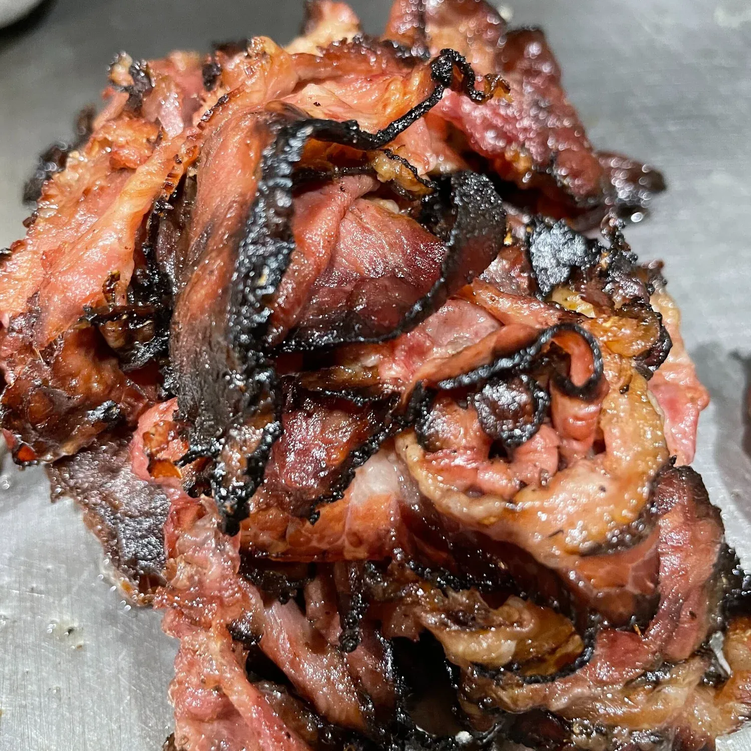 Close-up of a pile of thinly sliced pastrami with charred crispy edges on a metal surface