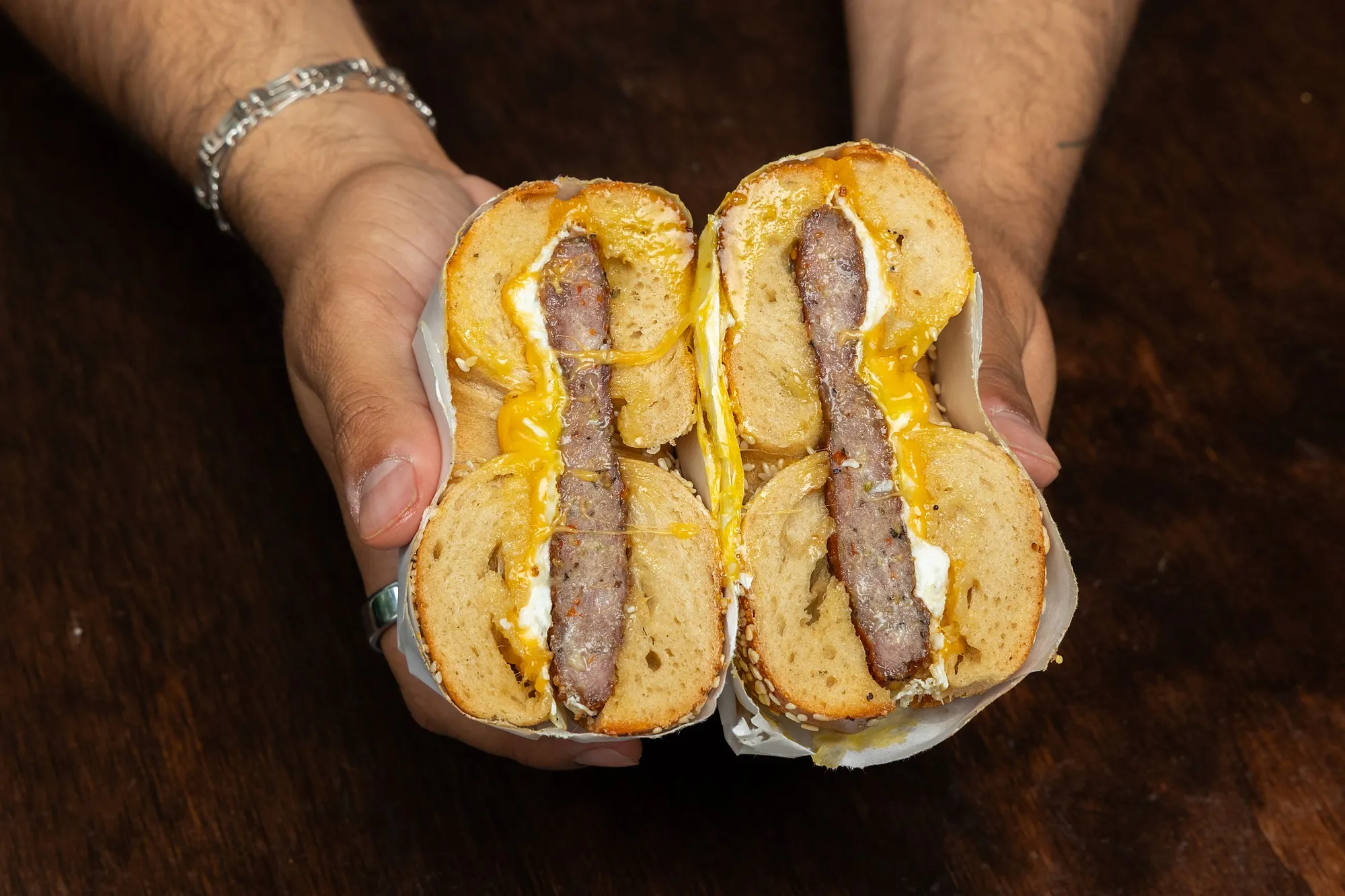 A Spicy Sausage, Egg & Cheddar on a sesame bagel, cut in half and held up in two hands