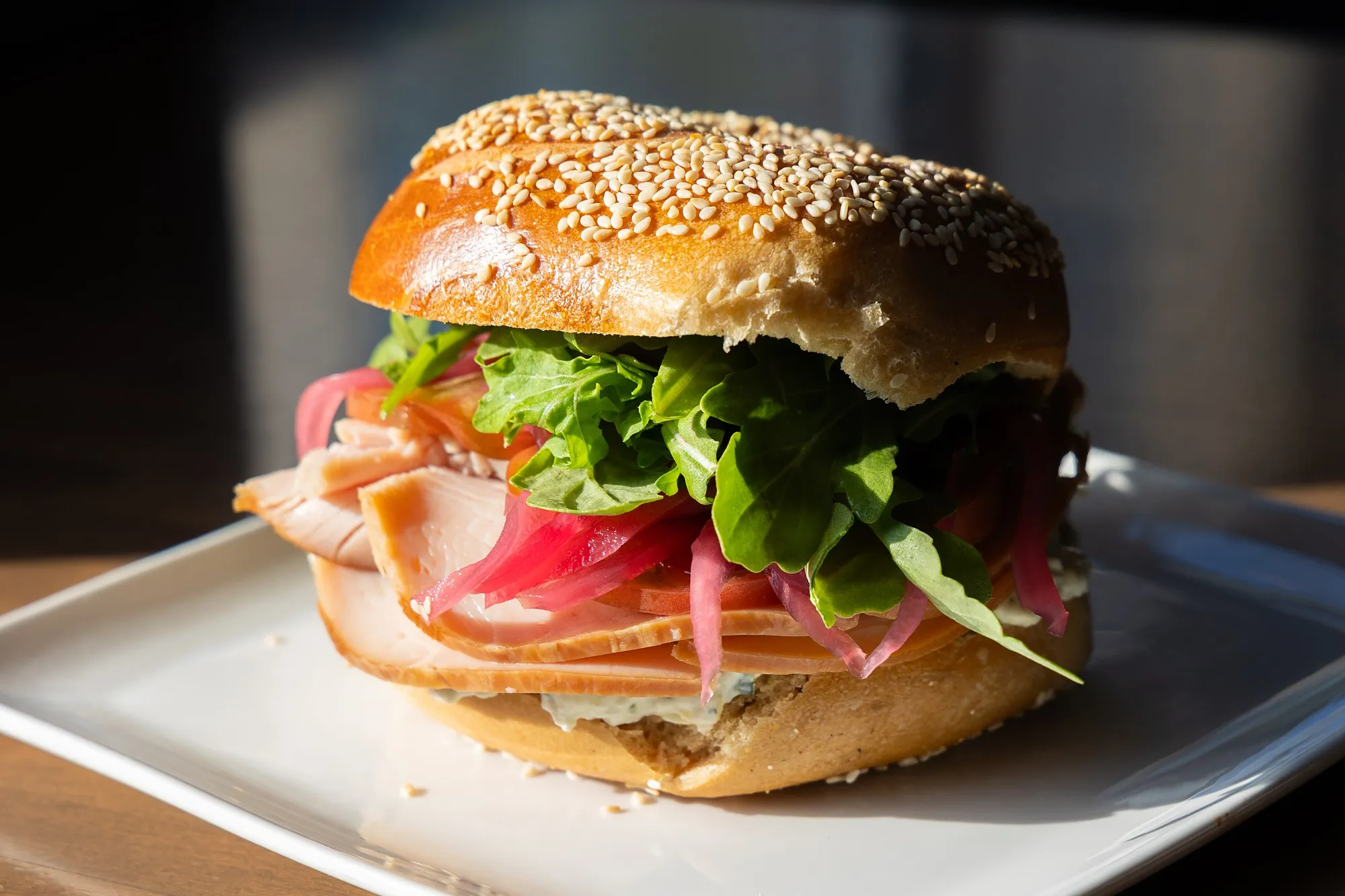 A turkey sandwich with arugula and pickled red onion on a sesame bagel