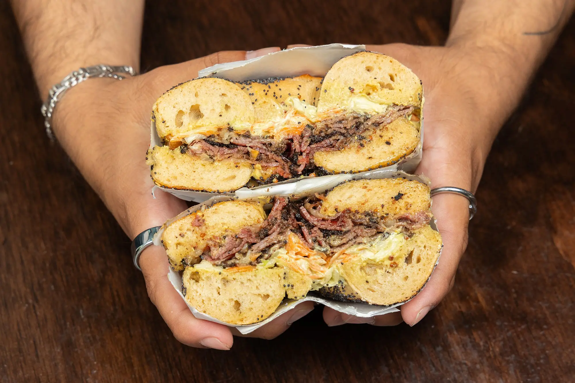 Williamsburg hot pastrami bagel sandwich held in two hands