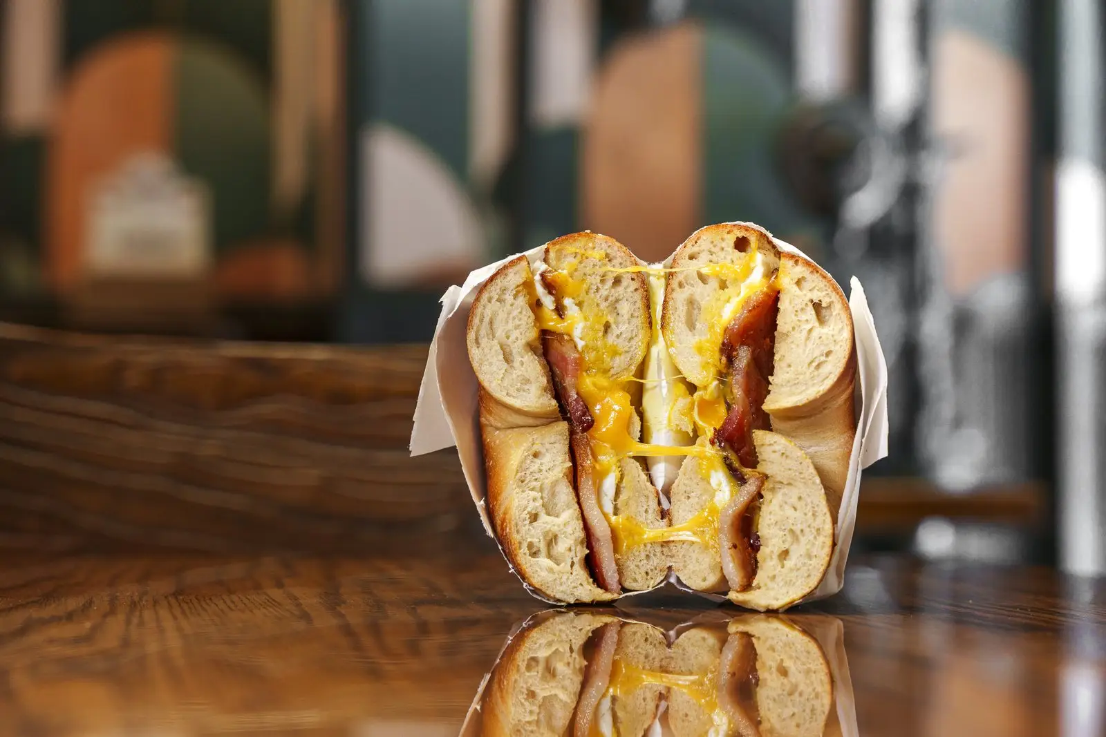 A Gotham bagel sandwich cut in half on a wooden table, melted cheese and giardiniera peppers showing in the cross-section