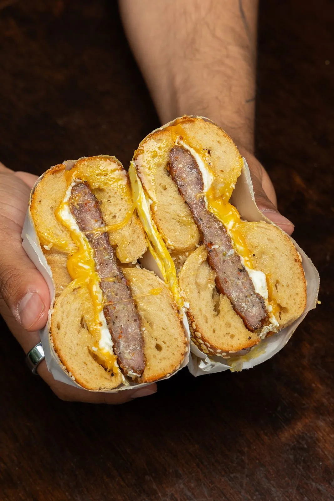 A spicy sausage, egg and cheddar bagel sandwich cut in half and held open
