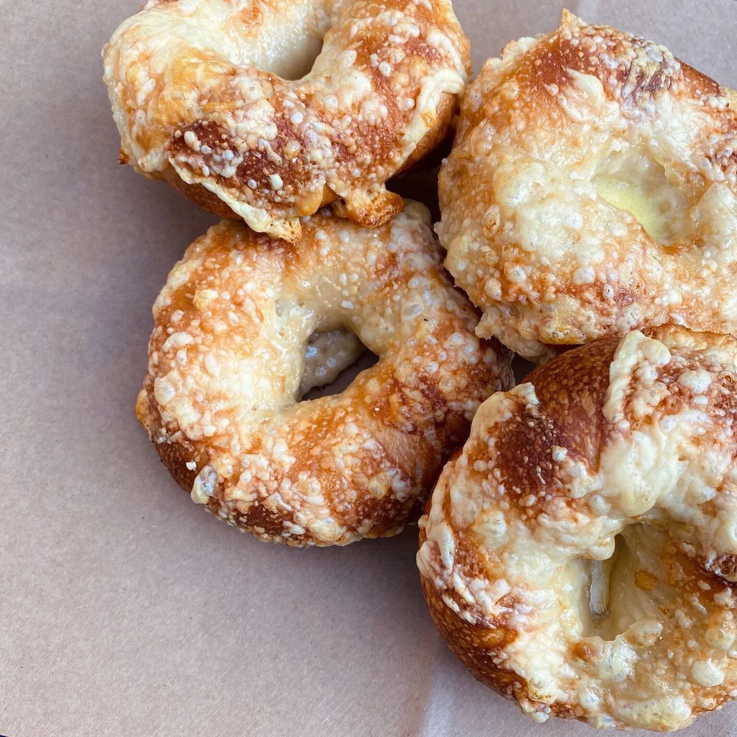 Four bagels topped with melted, browned asiago cheese on brown paper