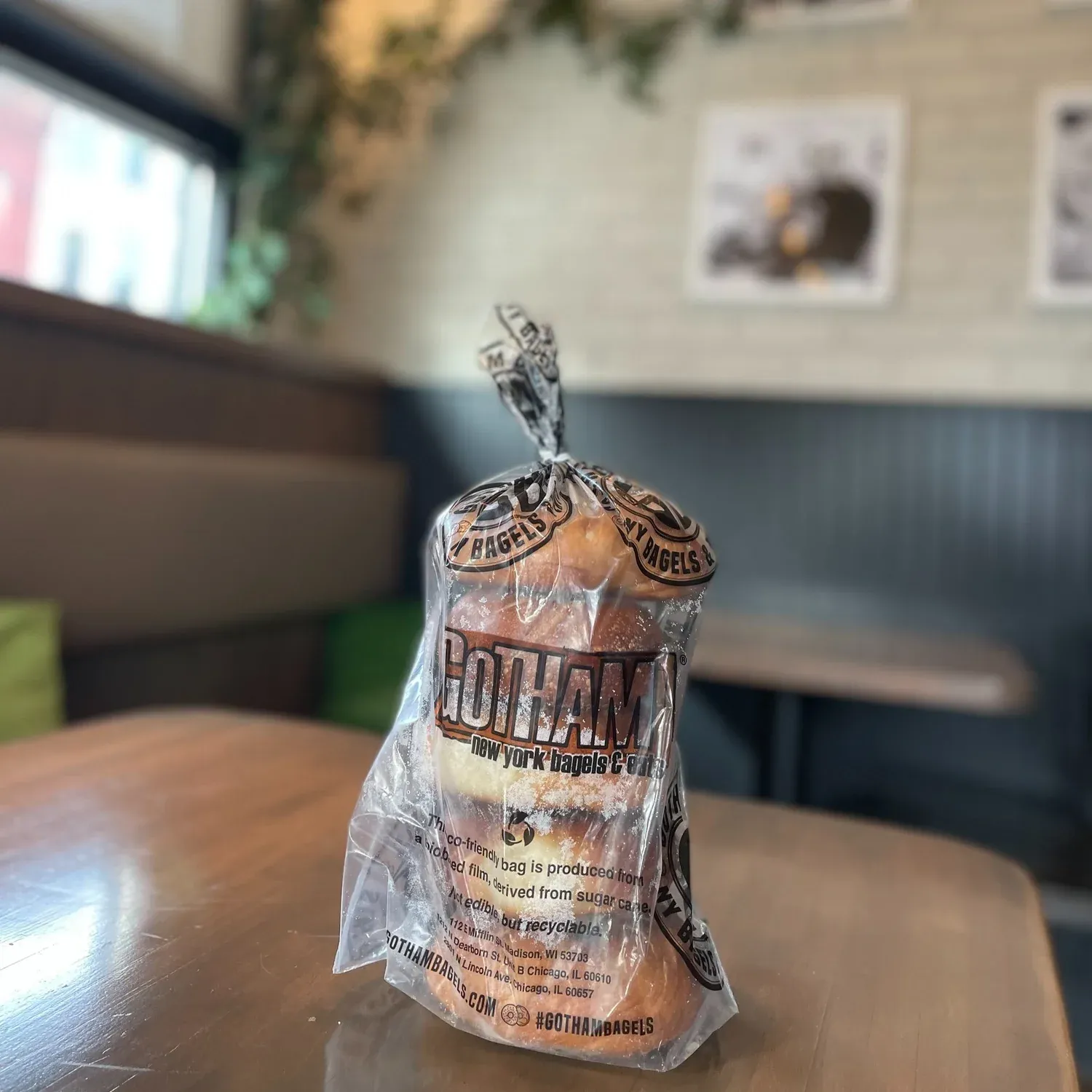Frost-covered bagels in a clear Gotham bag tied at the top, standing on a cafe table